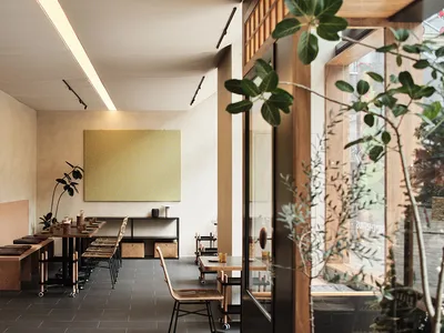 A modern restaurant interior featuring wooden tables, concrete flooring, and green plants
