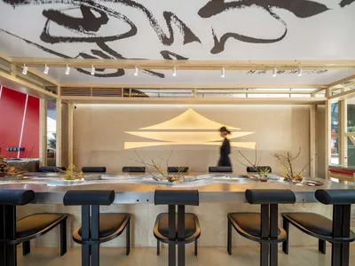 A modern restaurant interior with a wooden counter and sleek black seating.