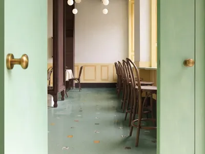 Green and minimalist restaurant interior with wallpaper and modern lighting fixtures.