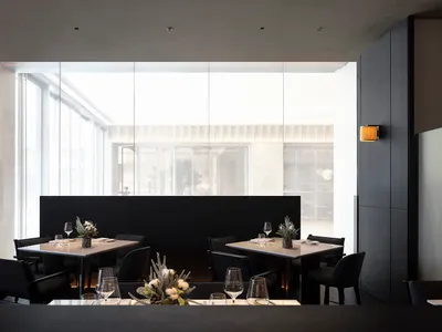 A modern restaurant interior featuring black metal and marble tables, chairs, and accents.