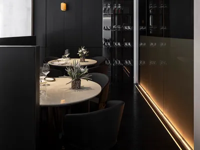 Modern dining room with black metallic wall featuring round tables and chairs, illuminated by subtle ambient lighting.