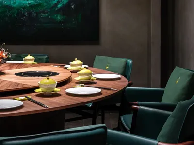 Modern restaurant interior featuring a round wooden dining table with green chairs and minimalist decor.