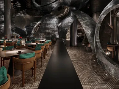 A modern, industrial restaurant interior with metallic and textured walls, featuring tables and chairs.