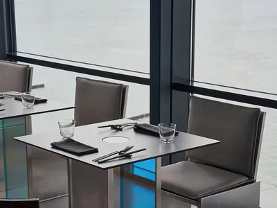 A modern restaurant with sleek metal and glass furniture and a waterfront view.
