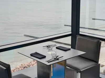 Modern restaurant setting with a metal table, leather chairs, and a stunning sea view.