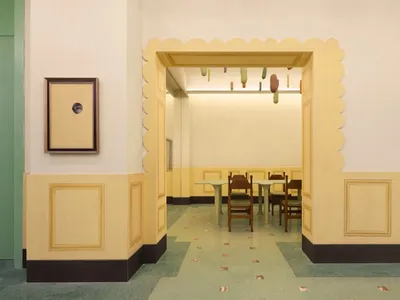 Interior of a cafeteria with yellow painted walls, wooden furniture, and green flooring.