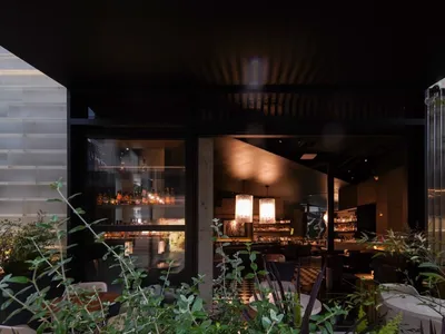 Modern restaurant interior with concrete walls, glass windows, and a bar area.