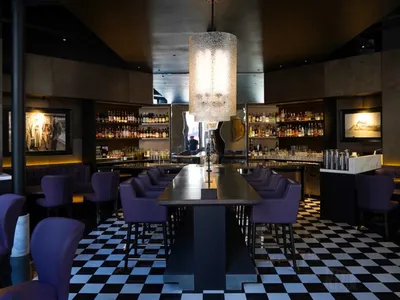 Interior of a modern bar featuring black marble countertops and a high ceiling with a large cylindrical light fixture.