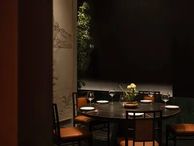 A round table with chairs and a centerpiece of flowers in a dimly lit industrial-style restaurant dining room with wooden ele