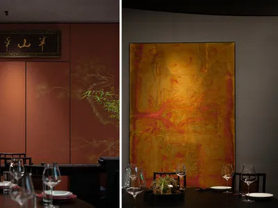 Metallic artwork hanging on a wall in a restaurant interior with a table and chairs.