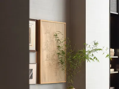 A minimalist living room with walnut furniture, a large frame on the wall, and green foliage in a vase.