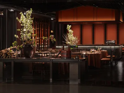 A modern restaurant bar features wooden furniture and dark metal fixtures.