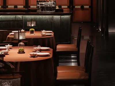 Modern restaurant interior with brown leather chairs, black wood accents, and dark, moody lighting.