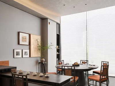 A modern restaurant interior featuring dark wood flooring, a round dining table, and art on the wall.