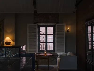 A cozy industrial living room with a wooden table, a white sofa, and a window with shutters.