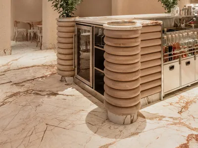 A modern bar area with a wooden counter, marble floor, and hanging wine bottles.