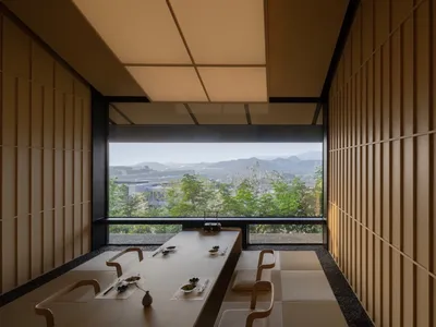 Modern restaurant interior with wooden walls and floor, large windows overlooking scenic landscape.