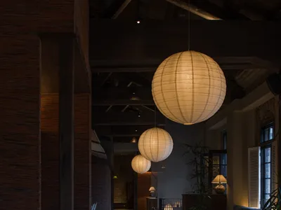 Industrial-style restaurant interior featuring hanging paper lanterns, wooden seating, and concrete flooring.