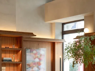 A modern restaurant interior with wooden furniture, green seating, and a large potted plant.