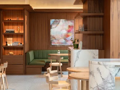 A modern restaurant interior with marble and wooden furniture, green leather seating, and abstract artwork on the wall.