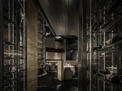 A modern industrial restaurant interior with metal shelving displaying bottles of wine and a dining area with tables and chai