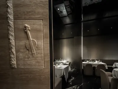 Modern restaurant interior with concrete walls and a violin wall art piece, featuring set dining tables and chairs.