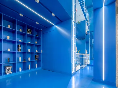 極簡藍色咖啡店室內，搭配金屬層架展示咖啡沖煮設備與配件。