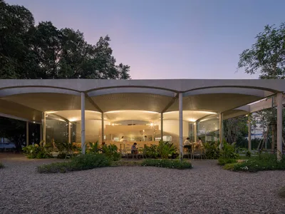 An illuminated restaurant with a modern design, featuring concrete structures and greenery.