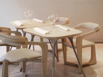 A modern restaurant interior with wooden tables and chairs, white walls, and circular light fixtures.