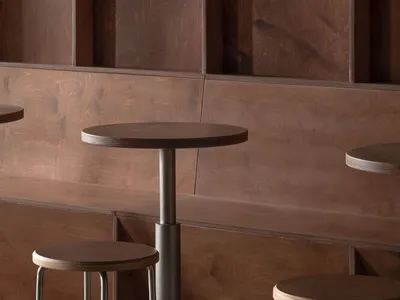 Modern café seating area featuring wooden stools and a round table with a concrete base, set against a wooden paneled wall.