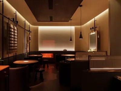 A minimalist restaurant interior with wooden tables, a glass partition, and warm lighting.