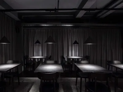 一間空蕩的極簡風格餐廳室內，配有金屬吊燈與木製餐桌。