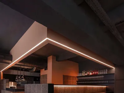 A modern bar interior featuring a concrete bar counter with wooden stools and warm lighting.