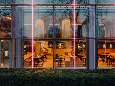 Contemporary restaurant with glass walls and wooden seating, illuminated by red neon lights.