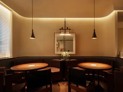 A modern restaurant dining room features round wooden tables with pendant lights, upholstered benches with leather accents, a