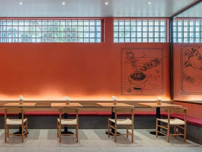 A modern restaurant interior with concrete walls, glass block windows, and wooden tables and chairs.