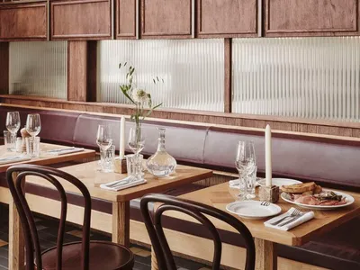 A modern restaurant interior with wooden tables, glass panels, and leather seating.