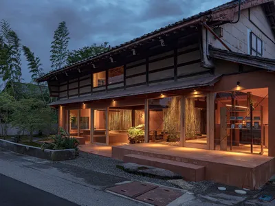 A traditional Japanese restaurant exterior illuminated at night with clay walls and a thatched roof, featuring a serene garde