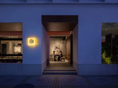 People sitting at a dining table in a modern restaurant interior with concrete walls and floor.