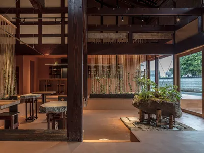 A spacious modern restaurant interior with wooden beams and tables adorned with plants.