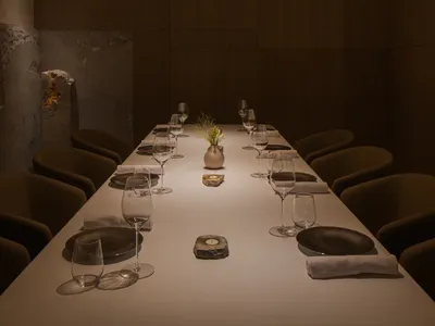 A modern restaurant dining room with wooden floors and hanging lights.