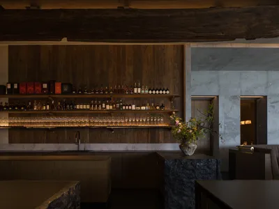 Modern restaurant bar with wooden shelves, marble and stone accents, and a flower arrangement.