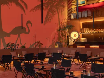 A modern restaurant bar with metal tables, wooden chairs, and glass decor.