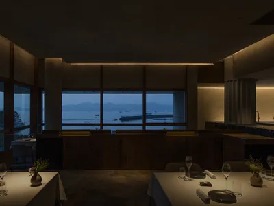 A spacious, well-lit interior of a modern restaurant that features a prominent view of the sea and mountains through large wi