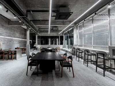 A modern restaurant interior featuring concrete and metal materials, with tables, chairs, and minimalistic design elements.
