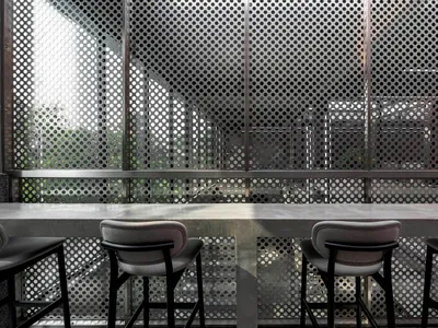 Modern restaurant bar featuring a concrete countertop, stools, and a perforated metal back wall.