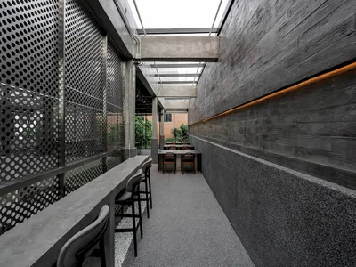 A modern restaurant interior featuring a textured concrete floor and walls adorned with perforated metal panels for light dif