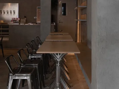 Industrial-themed restaurant interior with metal chairs, concrete pillars, brown wood elements, and white shelving.