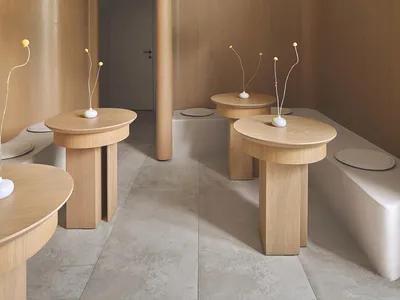 A minimalist restaurant interior with wooden tables and black pendant lights hanging from the ceiling.