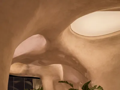 Modern restaurant interior with textured concrete walls and circular skylight.